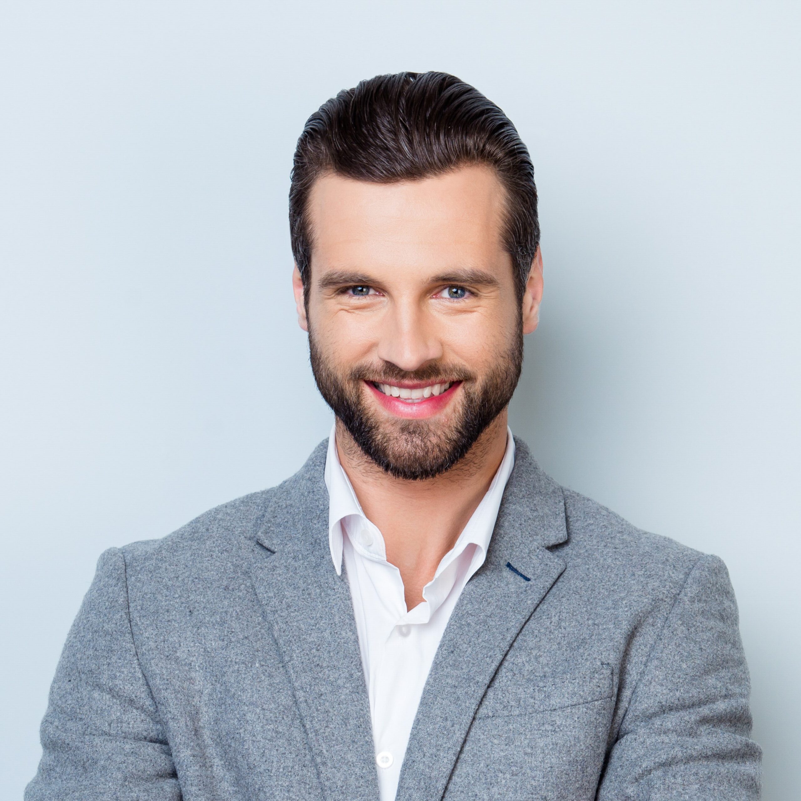 Portrait of happy with beaming smile freelancer in gray jacket standing with crossed hands against gray backdrop